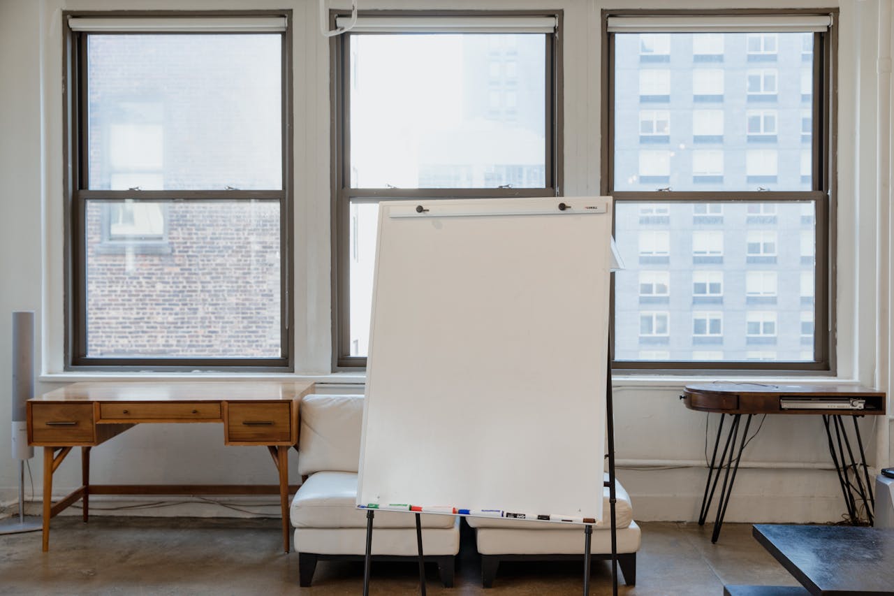 Bright minimalist office interior featuring a whiteboard, windows, and wooden desk.